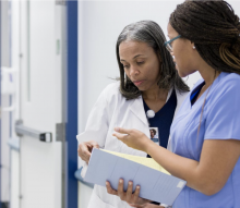 Nurse and doctor speaking in hallway looking over the contents of a folder. 